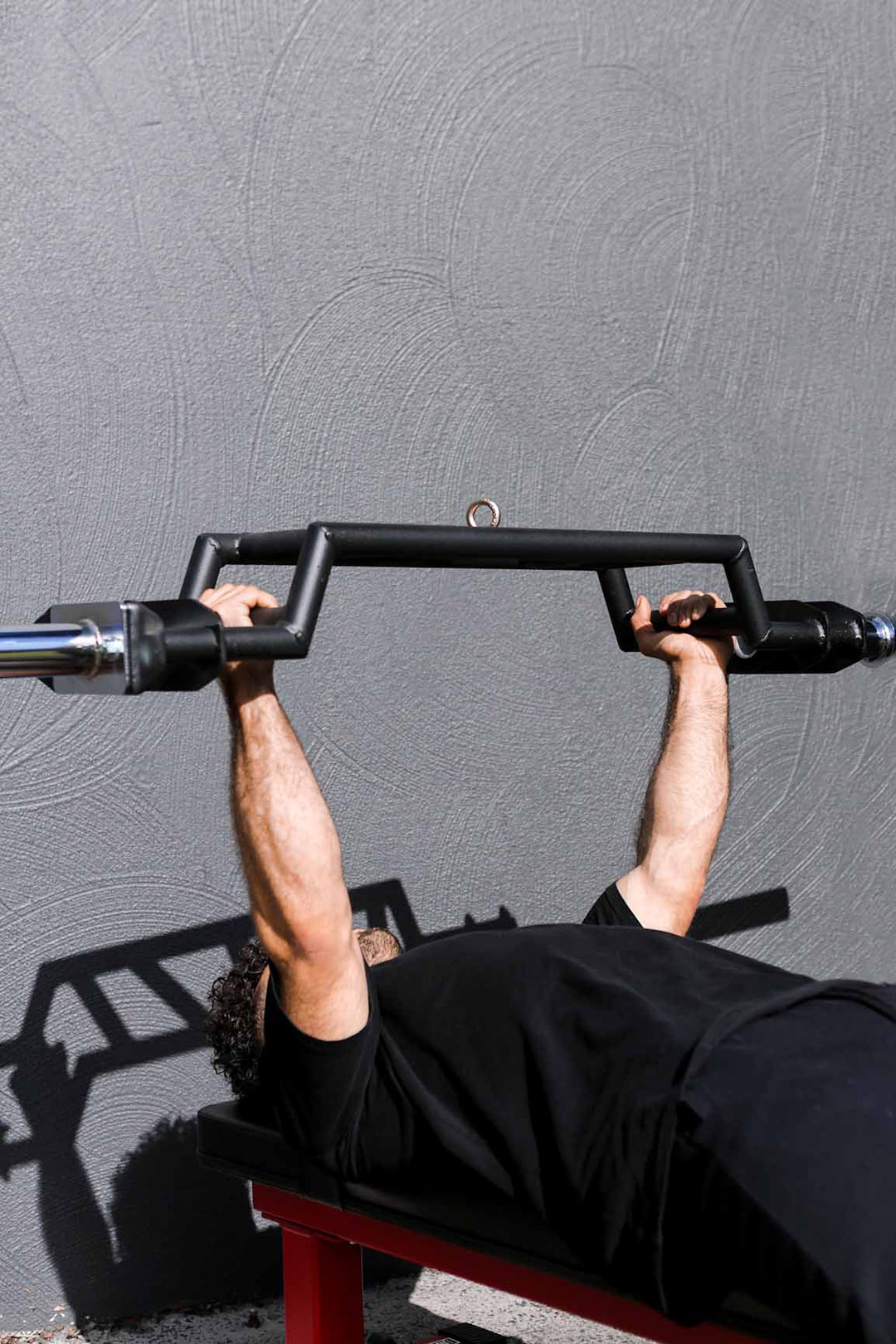 Man doing bench press with camebered swiss bar